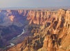Grand Canyon landscape with layered rock formations and a river winding through the deep canyon below under a hazy sky.