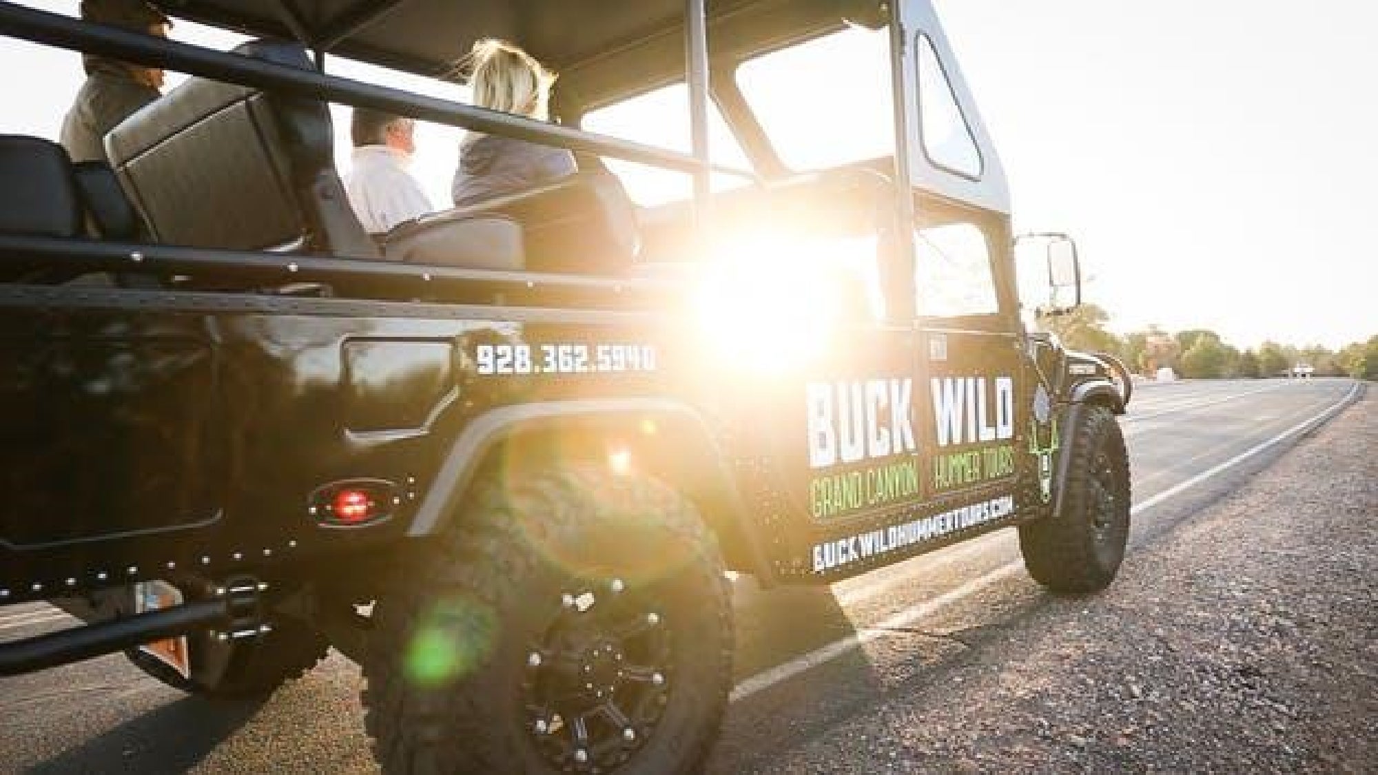 A black Buck Wild tour vehicle with passengers sits on a paved road at sunset, with sunlight shining through the open side.