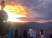 A group of people stand at a viewpoint taking photos of a dramatic sunset over the Grand Canyon with clouds in the sky.