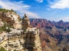 View of the Grand Canyon with layered rock formations, steep cliffs, and a wide canyon under a blue sky with some clouds.