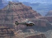 A helicopter flies over the layered rock formations of the Grand Canyon under clear skies.