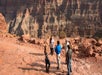 Five people stand and talk on a rocky ledge overlooking the steep cliffs and layered rock formations of the Grand Canyon.