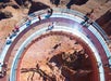 Visitors stand and walk on a curved, glass-bottomed skywalk extending over the edge of a canyon with steep rock formations visible below.