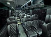 Interior of a luxury passenger van with black leather seats arranged in rows, overhead storage compartments, and subdued ceiling lighting.