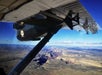 A view of the Grand Canyon landscape from an airplane, showing the plane’s wing and undercarriage against a clear blue sky.