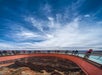People stand on a curved glass skywalk over a canyon under a blue sky with scattered clouds.