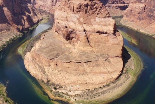 Aerial view of Horseshoe Bend, where the Colorado River curves around a large rock formation in a desert landscape.