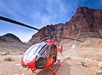 A red helicopter with the number 45 is parked on rocky terrain at the base of a canyon with layered cliff walls under a blue sky.