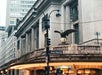 Street view of a building with a large eagle sculpture on the corner. Signs for Vanderbilt Ave and East 42nd St are visible. An illuminated marquee and a streetlight are in the foreground.