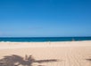 An empty beach with light colored sand and deep blue ocean water in the background on a sunny day.