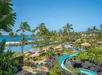 A tropical resort with palm trees, a pool, a winding water slide, and cabanas near the ocean under a clear blue sky.