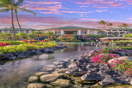 A tropical resort with lush gardens, palm trees, a pond with rocks and flowers, and a large building under a colorful sunset sky.