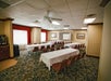 A conference room with two long tables arranged in a U-shape, covered with white tablecloths, and surrounded by red chairs. The room has carpet flooring and framed artwork on the walls.