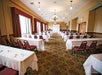 A conference room with rows of tables and chairs, white tablecloths, and a floral carpet under chandeliers.