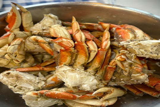 A stainless steel bowl filled with cooked and cracked crab legs and claws, showing red and white shells.