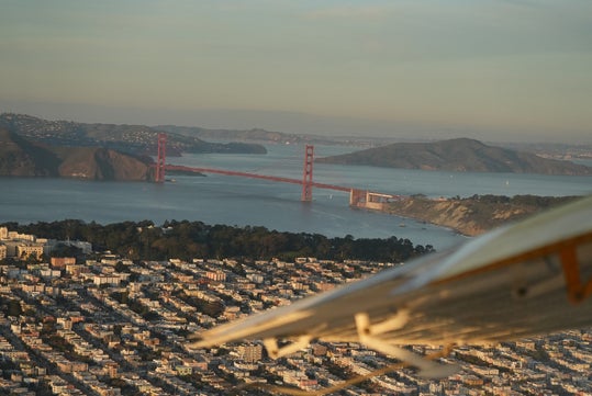 Aerial view of San Francisco with the Golden Gate Bridge in the background and part of an airplane wing visible in the foreground.