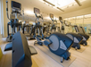 A gym with modern workout equipment, including elliptical machines and treadmills, arranged in rows on a wooden floor.