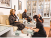People enjoying pedicures at a spa, sitting in chairs with foot baths. Spa workers attend to a woman and a man, while another woman engages in conversation nearby. Everyone is wearing robes.