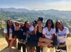 A group of woman holding a man in front of them and posing for a photo with Griffith Park behind them on a sunny day.