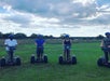 Four tourists wearing helmets and riding segways in a bright green field on a cloudy day on the Guided Segway Tour of Lake Louisa State Park.