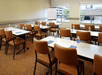A conference room with white tables with brown leather chairs at them lined up in front of two windows and a whiteboard.