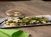 A salad with spinach, eggs, berries, chicken, and nuts on a white plate with a silver fork to the left.