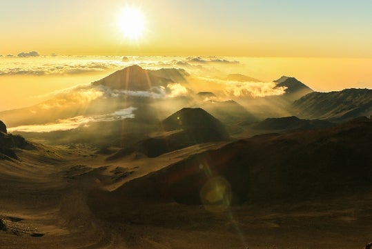 The sun just above the horizon shining down on some mountains on the Haleakala Sunrise Tour in Wailuku Hawaii, USA.