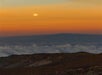 The full moon within the early sunrise over the clouds and mountains on the Haleakala Sunrise Tour in Wailuku Hawaii, USA.