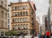 A busy city street with cars and pedestrians in front of a historic multi-story building housing a Duane Reade pharmacy on the ground floor.