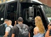 Several people with backpacks stand in line and board a black bus parked on a city street.