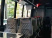 Rows of black leather, diamond-stitched seats inside a modern bus or coach, with cup holders and large windows on one side.