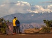 A couple overlooking Shafer Trail on a tour of the Island in the Sky district of Canyonlands National Park with clouds in the distance.