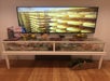 Glass display case with cheese products and memorabilia; TV above shows cheese wheels on racks.