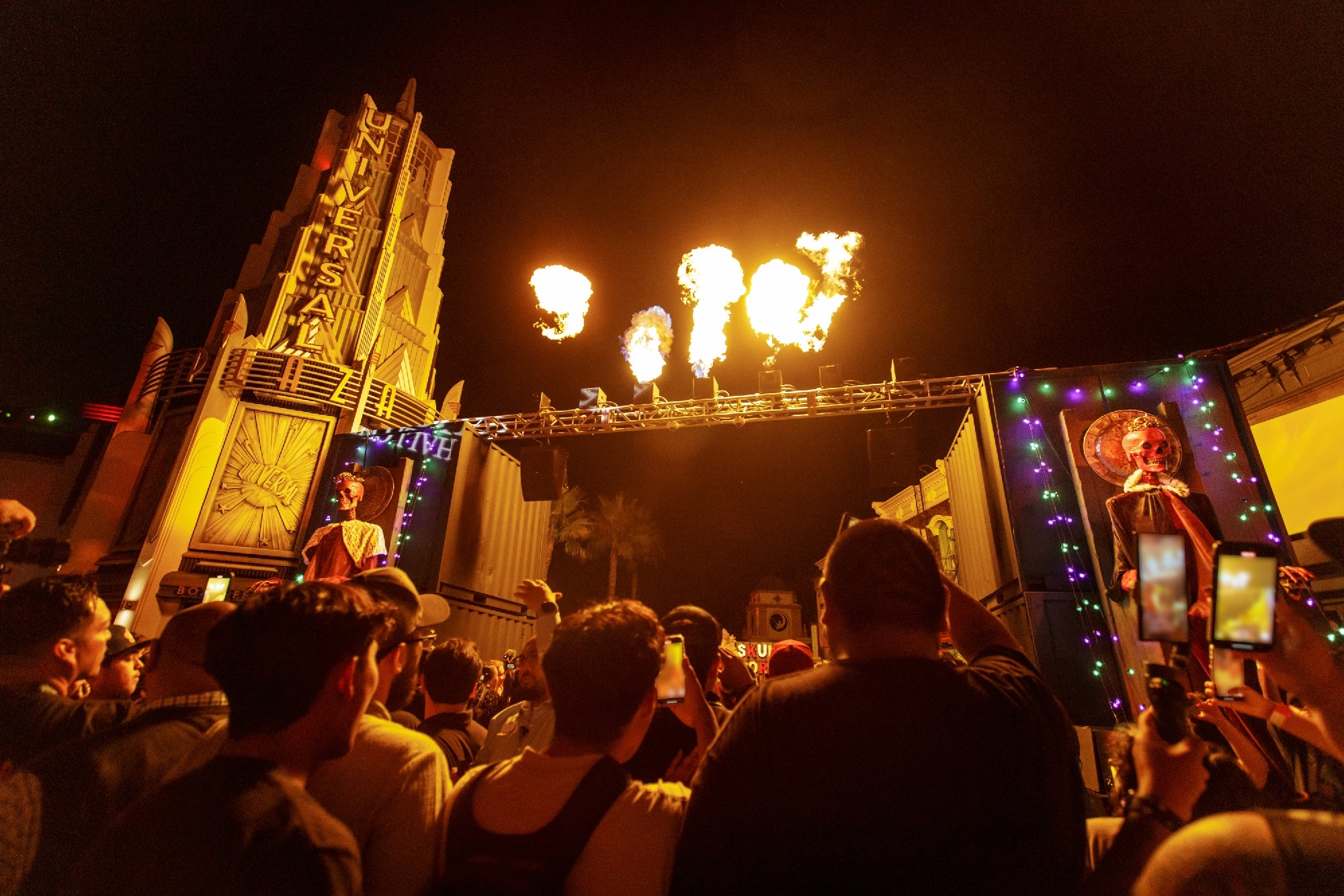 A crowd watches a nighttime outdoor show with fire effects on stage at Universal Studios, with neon lights and signs in the background.