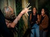 A performer in a mummy style costume with their arm out scaring two young women who have their mouth open wide screaming.