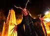 A performer in a bloody mask with no eyes and deer like antler, a long black robe, and bloody hands with long fingers.