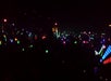 A dark concert venue with a crowd holding various colorful glow sticks and LED lights, creating a vibrant display in the darkness.