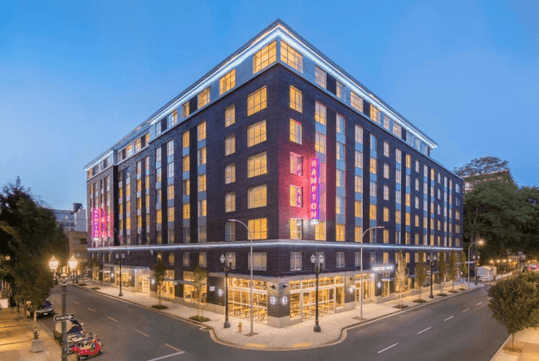 Street view of two sides of the exterior of the Hampton Inn and Suites by Hilton Portland-Pearl District at dusk.