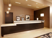 A modern hotel reception area with a dark wooden desk, three hanging spherical lights, framed pictures on the wall, and a table lamp on the counter.