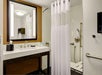 A modern bathroom with a double sink, large mirror, and shower area with a white curtain. There are support bars and a shower chair, indicating accessibility features.