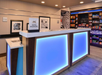 Hotel reception desk with blue lighting, Hilton Honors sign, framed artwork on walls, and a snack area with various items displayed on shelves in the background.