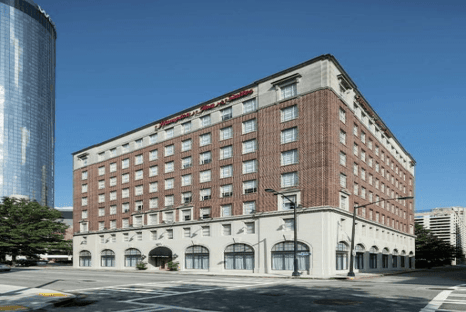 Red-brick hotel building with eight floors and arched windows on the lower level, situated on a city street corner under a clear blue sky.