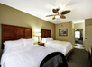 Two queen beds, a nightstand with a lamp in between, and a ceiling fan