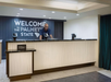 A hotel front desk clerk stands behind a counter with a "Welcome to the Palmetto State" sign and Hilton branding on the front.