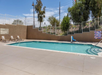 Outdoor swimming pool with two lounge chairs, a lift, and surrounding fence under a clear sky.