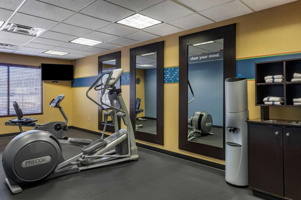 A gym room with exercise equipment, including a stationary bike and an elliptical machine, mirrors on the wall, a water cooler, and shelving with towels.