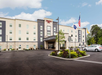 Exterior view of a four-story hotel with a sign above the entrance, American and state flags flying, and a parking lot with cars in front.