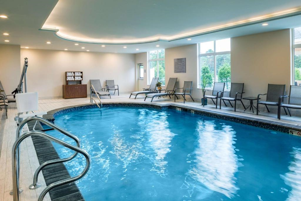 Indoor swimming pool with surrounding lounge chairs, a small towel station, and large windows showing greenery outside.