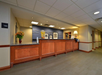 Hotel reception area with a wooden counter, a flower vase, a water dispenser, and framed pictures on the wall.