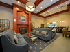 Hotel lobby with gray sofas, a fireplace, and modern lighting. A painting hangs above the fireplace, and there's a dining area with tables and chairs in the background.